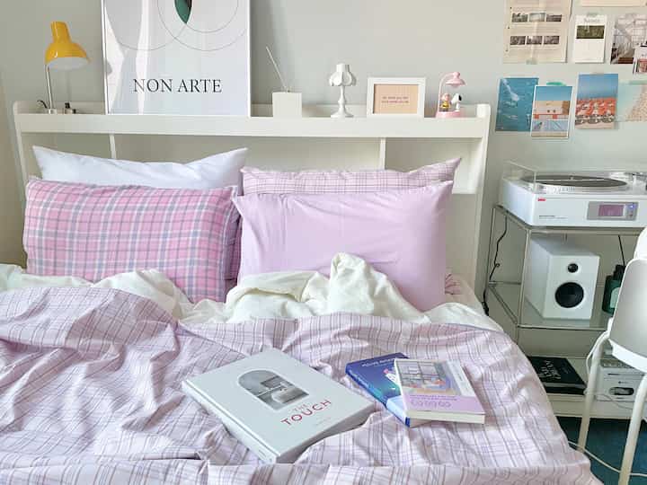 Studio bedroom with light beige walls and pink check pillows, books for reading placed on bed