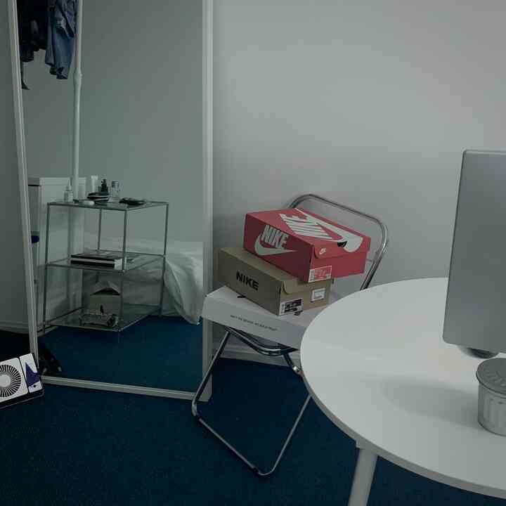 Modern compact room with white walls, round dining table, blue rug, transparent folding chair, and orange/red boxes stacked