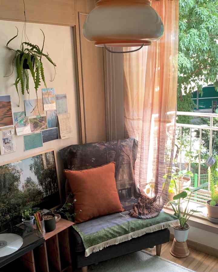 暖かいブラウンとオレンジの色調のリビング、クッションやカーテン、植物が配置され、居心地の良いバルコニーが見える雰囲気あるインテリア