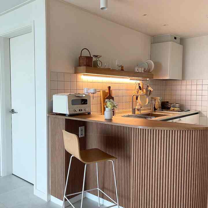 Compact kitchen space featuring white and wood tones with warm ambient under-shelf lighting creating a cozy atmosphere