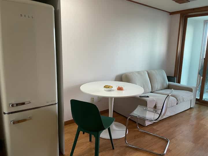 A compact and modern dining room in white and green tones, featuring a beige sofa and a round table