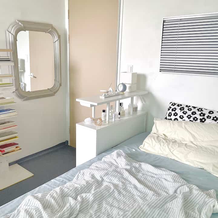 A white and sky blue bedroom featuring neat bedding, a console table, and wall-mounted blinds creating a clean atmosphere