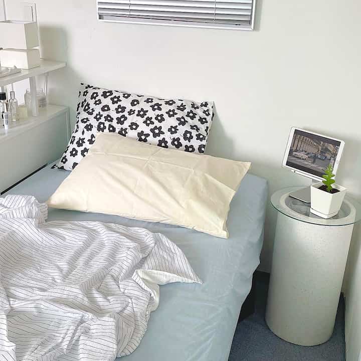 White-walled minimal bedroom featuring black floral pillows and striped bedding with a clean atmosphere