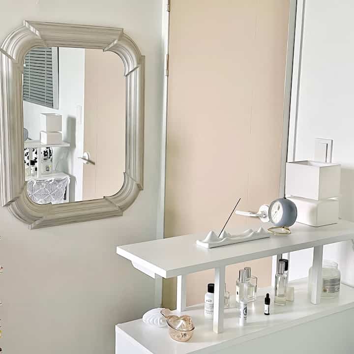 A simple powder room in white and beige tones featuring a wall mirror and neatly arranged accessories