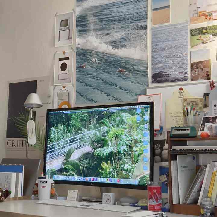 White and wood-toned studio home office featuring a desk with a large monitor, posters, and decorative objets creating a cozy workspace