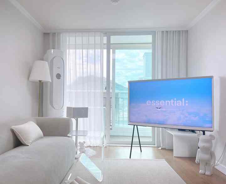 明るいホワイトトーンの20坪台リビング、透明なアクリルテーブルとセリフテレビ、ソファが配置された清潔で広々とした印象的な空間