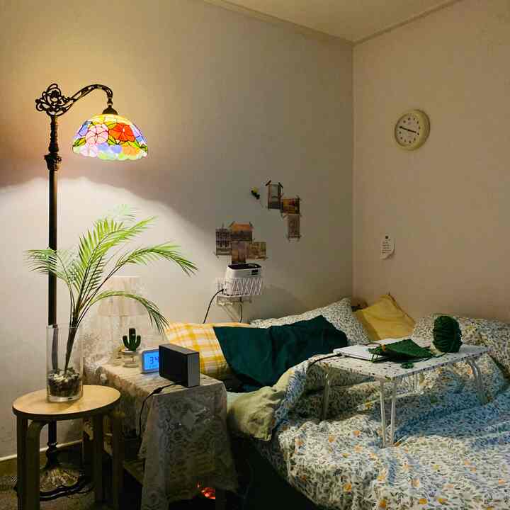 イエローとグリーンの色調が調和した狭い寝室、ヴィンテージのステンドグラスフロアランプとアレカヤシが配置された雰囲気のある空間