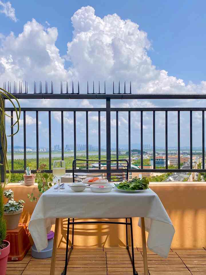 Bright white and wood tones blend in a veranda space featuring an outdoor table and chair, tablecloth, and plants creating a cozy home cafe vibe