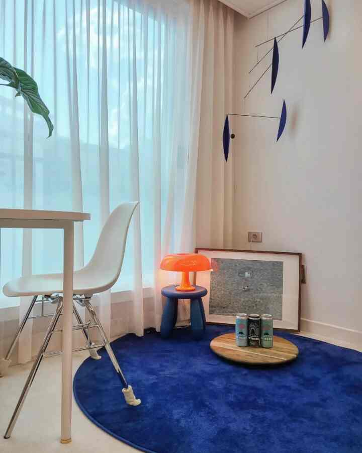 Bright natural dining room with white curtains and chair, featuring a round blue rug and an orange table lamp as accents