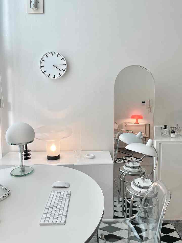 Modern white-tone home office featuring a round desk, wall clock, and stylish lamps in a clean interior