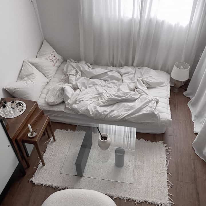 Calm ivory-toned studio bedroom featuring soft bedding, sheer curtains, wooden furniture, creating a simple and modern atmosphere