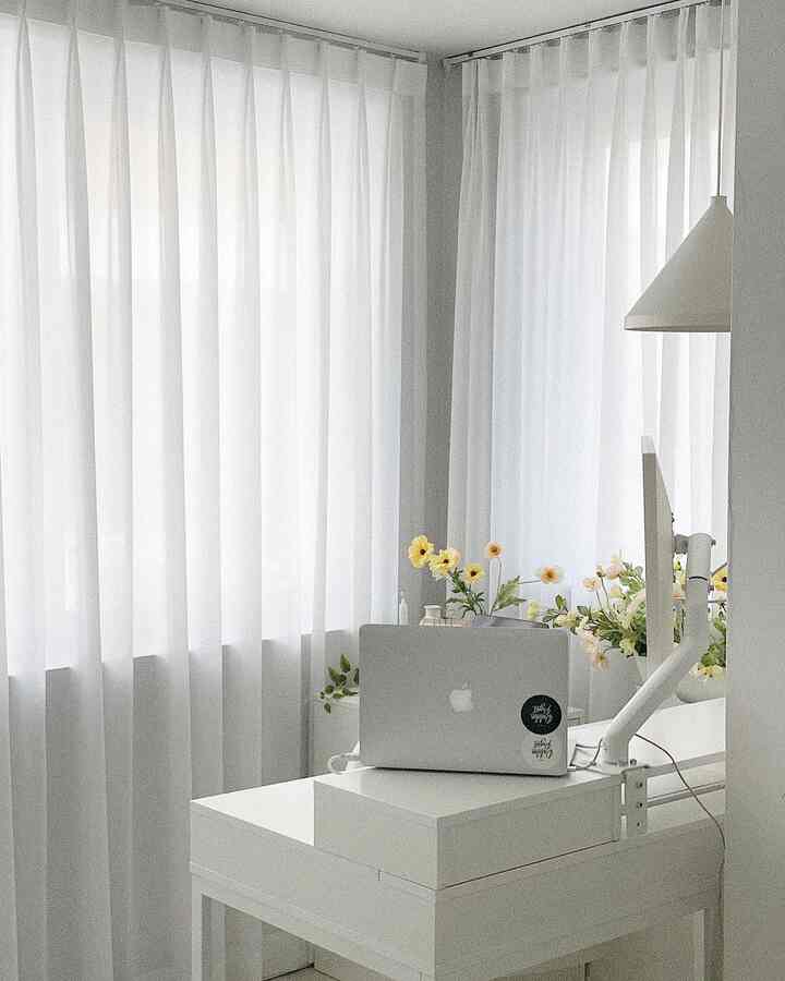Bright white-toned home office featuring a white desk with MacBook Pro in a clean and luminous setting