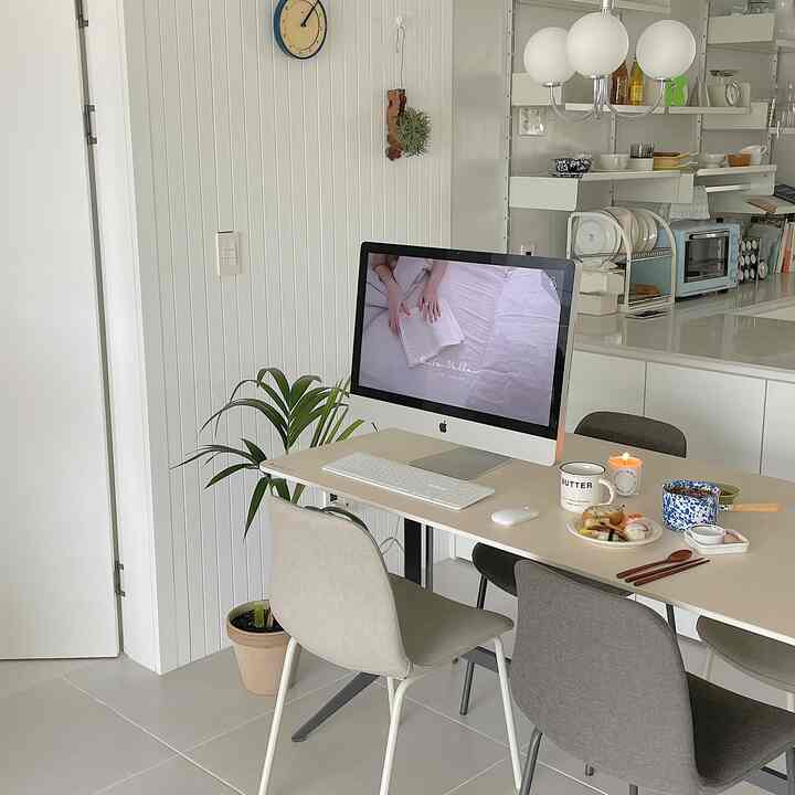 ナチュラルとホワイトトーンのキッチン兼ホームオフィス空間、ダイニングテーブルにiMac、寿司、キャンドル、マグカップが配置された温かみのあるインテリア