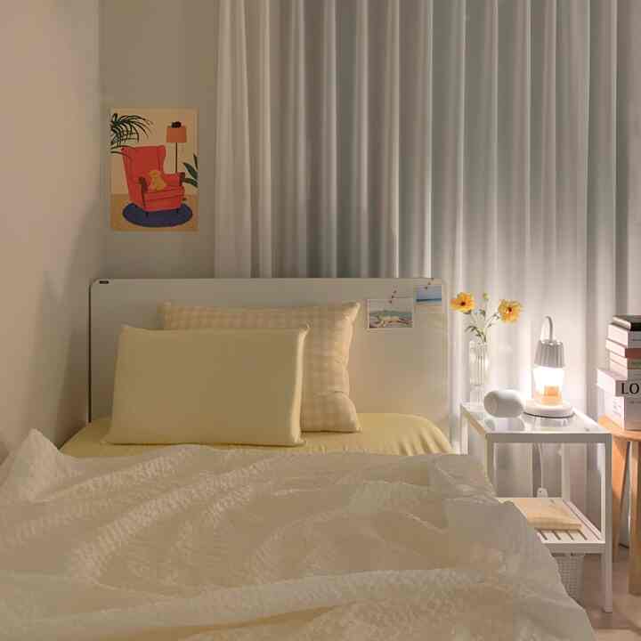 白と黄色のトーンの寝室、清潔感のあるナイトテーブルと花の装飾が配置された落ち着いた雰囲気の空間