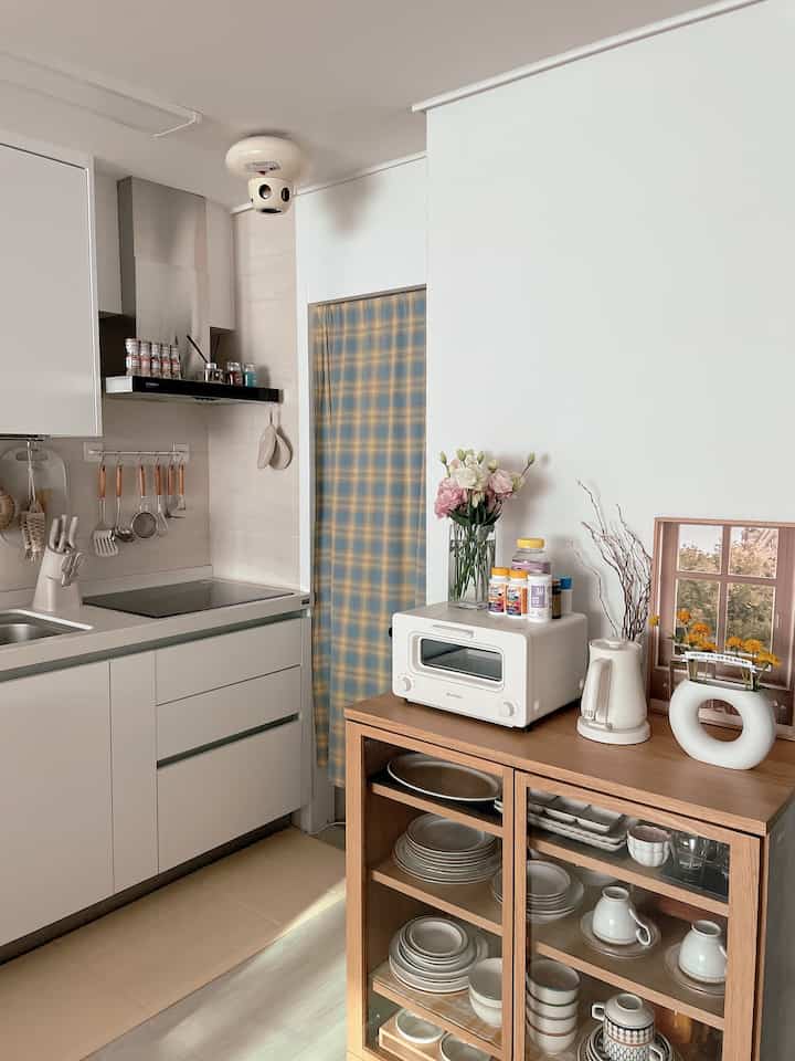 A compact kitchen space in white and wood tones, featuring neat storage and home cafe appliances creating a cozy atmosphere