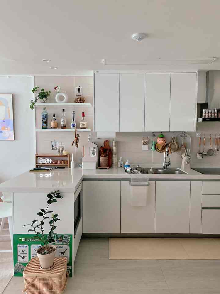 White and natural toned kitchen featuring white cabinets and countertops, rattan baskets, and kitchen utensils creating a clean and warm atmosphere