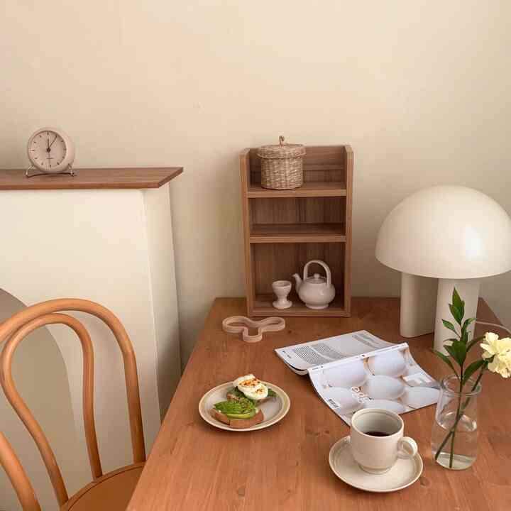 A cozy home cafe space featuring warm wood tones and beige walls, with a dining table, chair, charming accessories, and soft lighting.