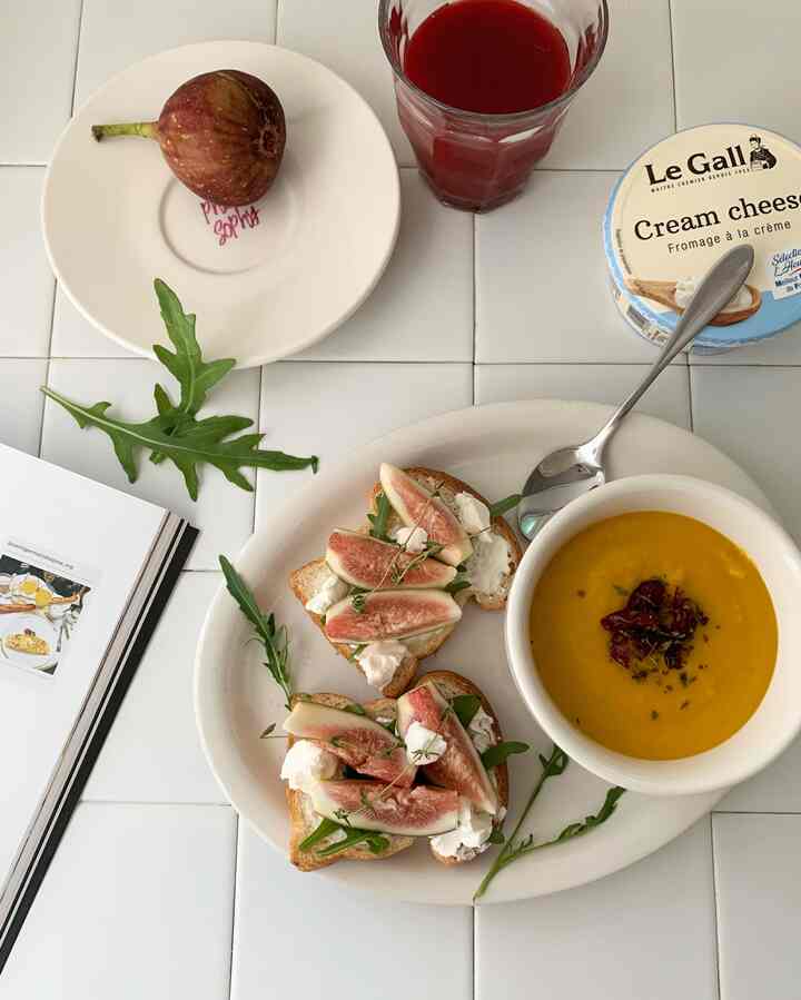 Cozy home cafe meal on white tiled table featuring fig toast with cream cheese and a glass of red juice