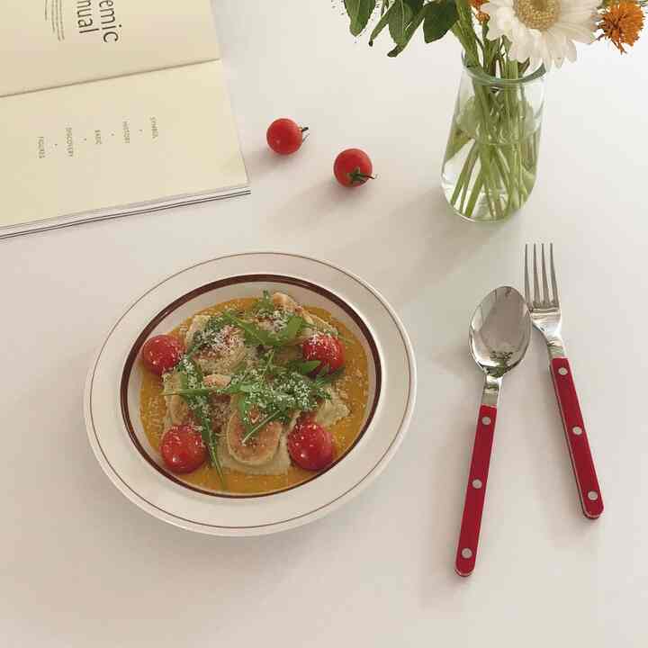 Clean home cafe table with red-handled cutlery, vase with flowers, and plated food on white background