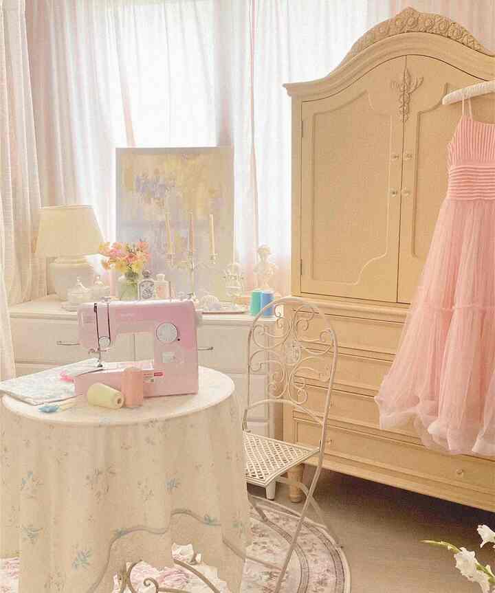 柔らかなピンクとベージュのトーンが印象的なウォークインクローゼット。ピンクのミシンとクラシックな丸テーブル、ワードローブが配置された落ち着いた空間
