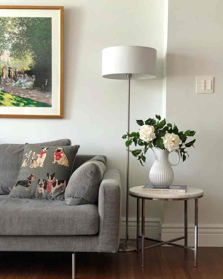Gray and white toned living room featuring a sofa, side table with vase of flowers, and floor lamp in a simple setting