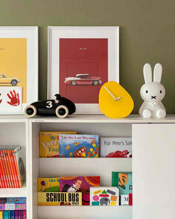 Children's room with light green wall background, white bookshelf topped with yellow clock, bunny lamp, and toy car