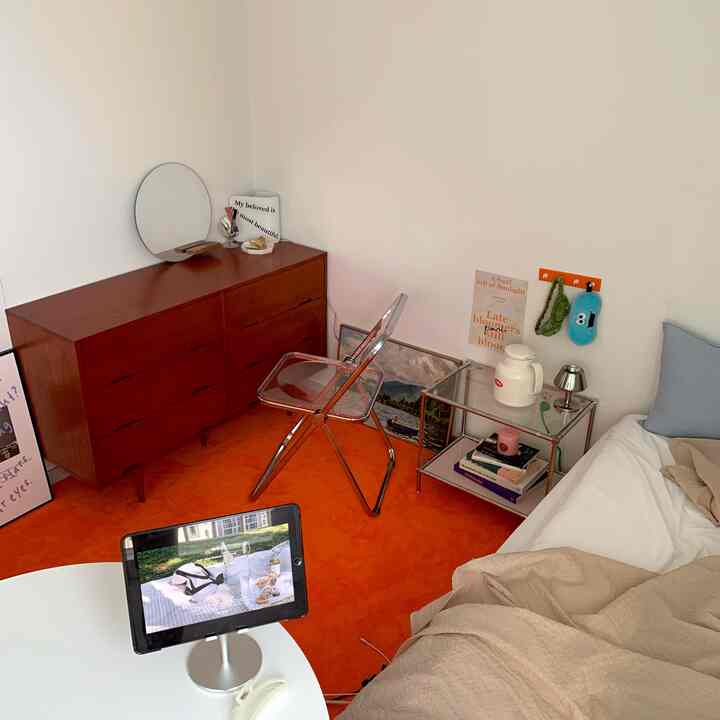 Warm orange rug and modern wooden dresser with transparent stool in a single household studio bedroom space