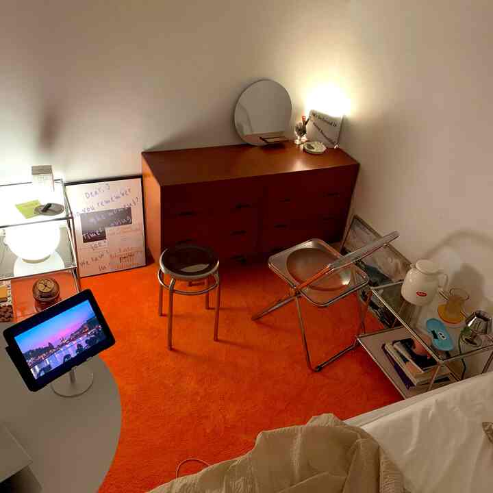 Studio bedroom featuring a bright orange rug, brown dresser, stools, and modern minimalist interior
