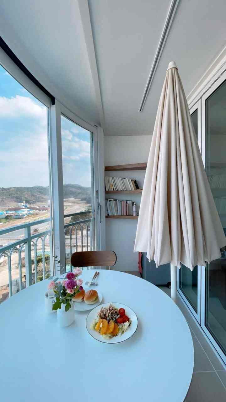 White and wood-toned veranda space featuring shelves and round table, creating a cozy home cafe atmosphere
