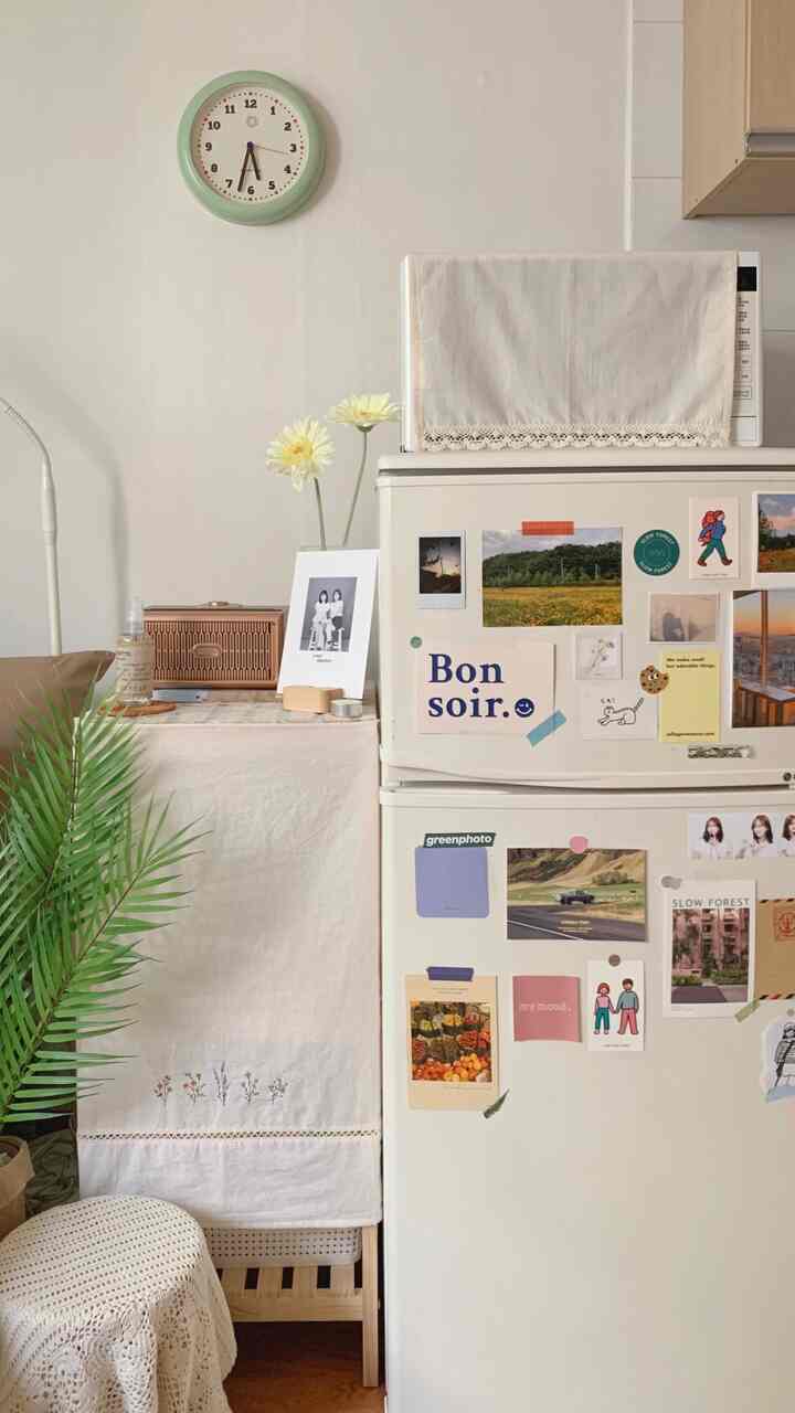 White and natural toned kitchen space featuring a refrigerator decorated with various postcards and photos, creating a cozy atmosphere