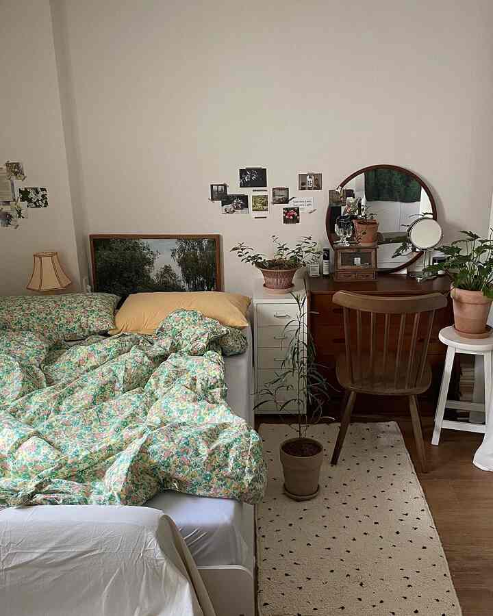 ベージュの壁と木製家具の寝室、花柄の掛け布団と複数の植物が配置された温かみのある空間