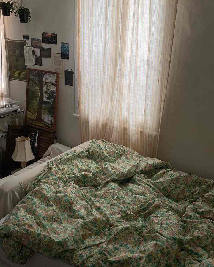 ナチュラルな色調の寝室、花柄の寝具とカーテン、ビンテージ感のある壁装飾が印象的な空間