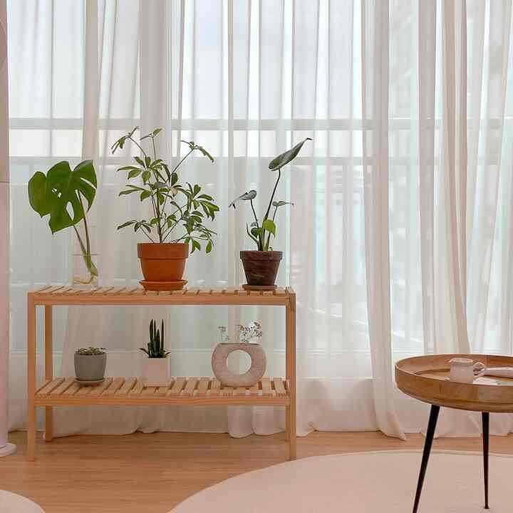 Natural and simple living room with white sheer curtains and wood-tone shelf featuring plants