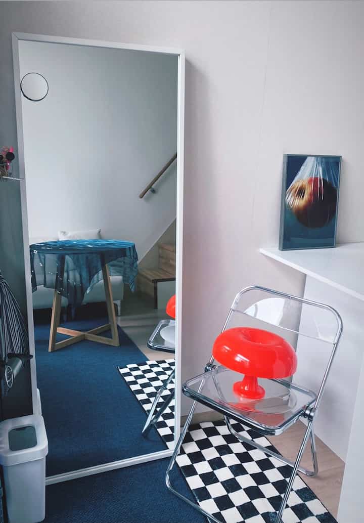 Blue and white toned entrance area featuring a large mirror and a transparent chair with a bright red lamp accessory on top, modern vibe