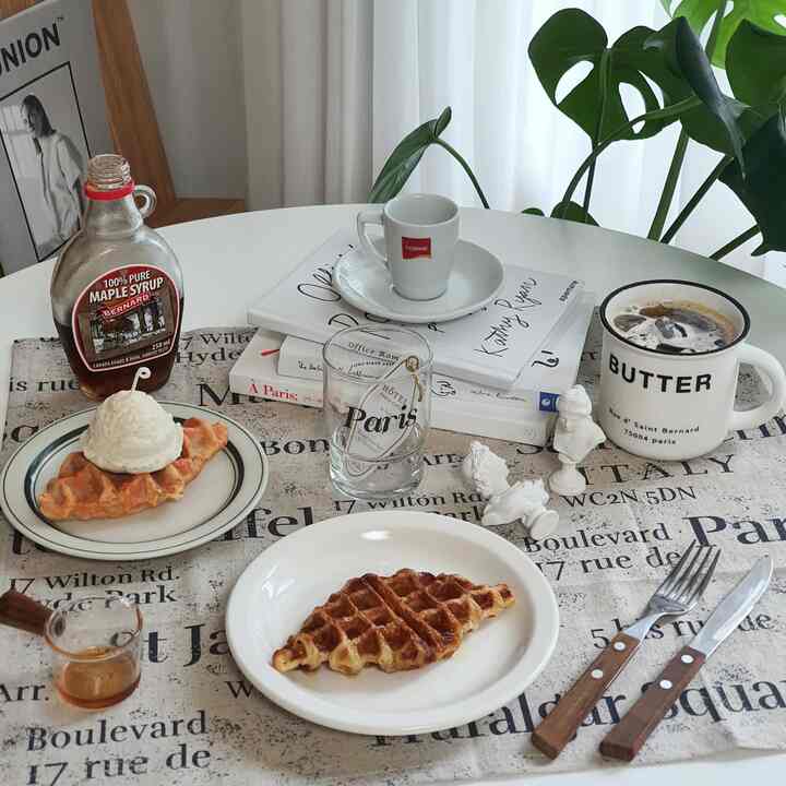 Cozy home cafe scene with white French lettering placemat featuring waffles, ice cream, coffee, and cups on a white table