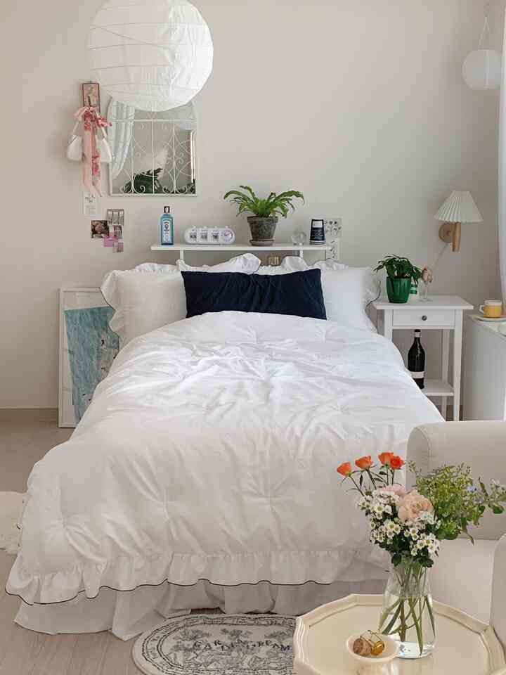 白色調の寝室空間、フレンチカントリースタイルのヴィンテージベッドとナイトテーブル、植物が配置された暖かな雰囲気のインテリア