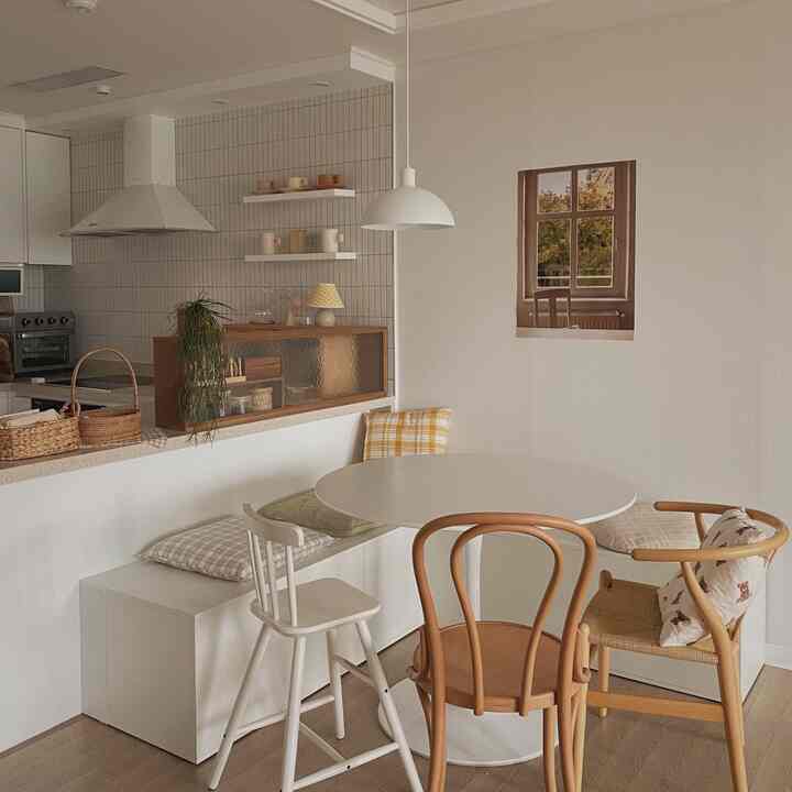 白とベージュ色調のキッチン、丸いダイニングテーブルと多様な椅子とクッションが配置されたナチュラルモダンな空間