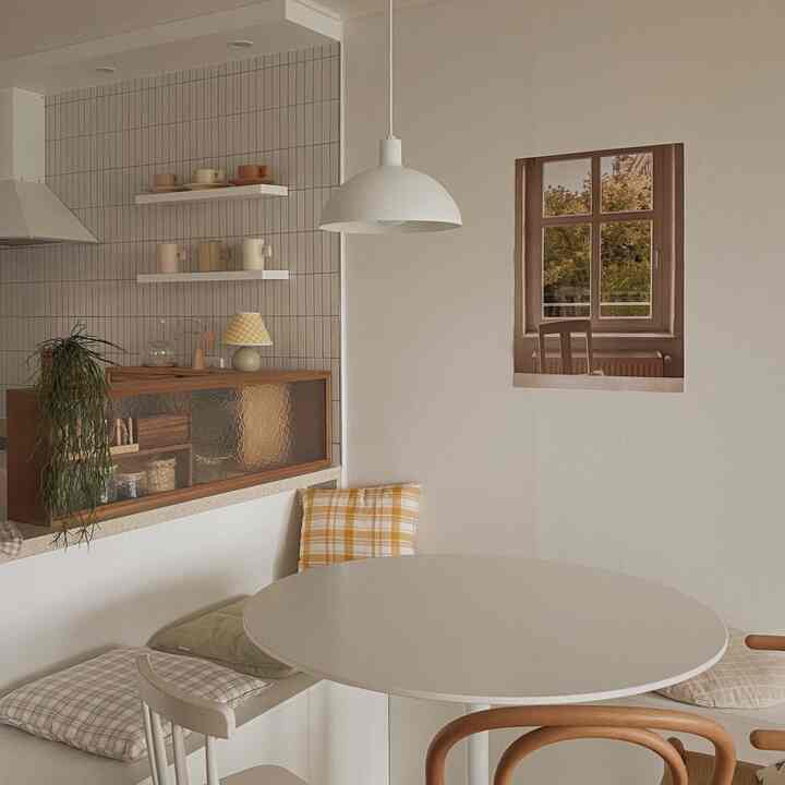 Beige and white toned kitchen-dining area featuring a round dining table, assorted chairs, wall shelves, and cushions creating a cozy cafe style interior