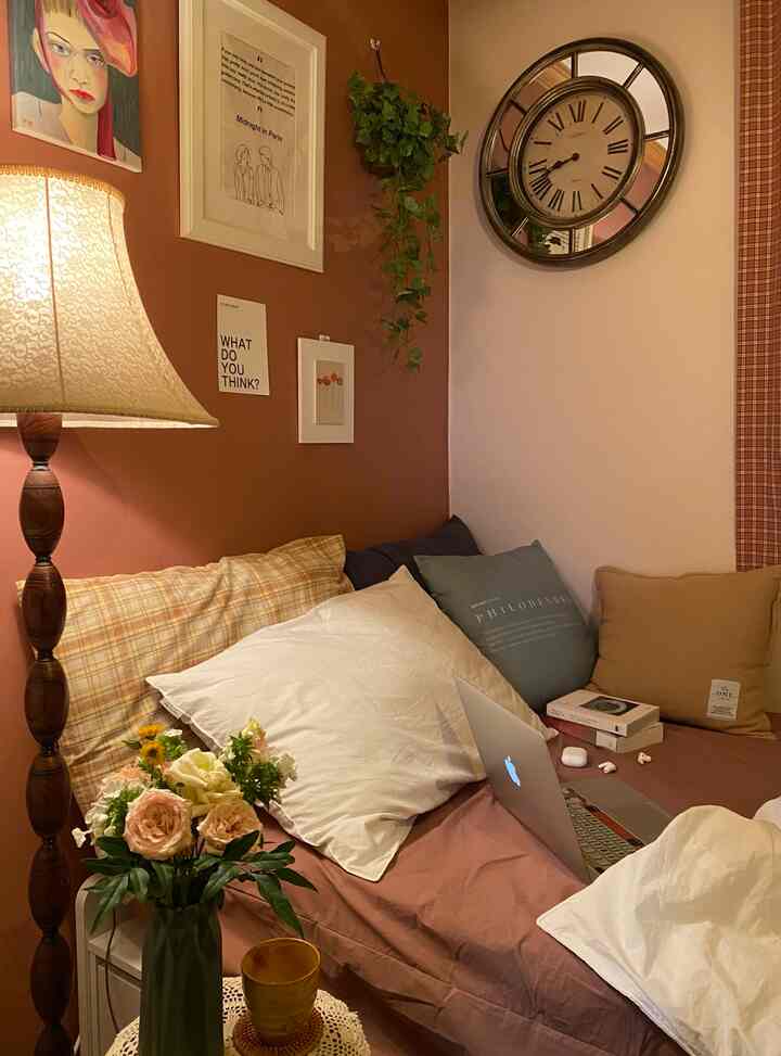 ピンクとライトブラウンの色調の寝室、壁掛け時計と絵画、フロアランプ、花瓶が配置された雰囲気のあるインテリア