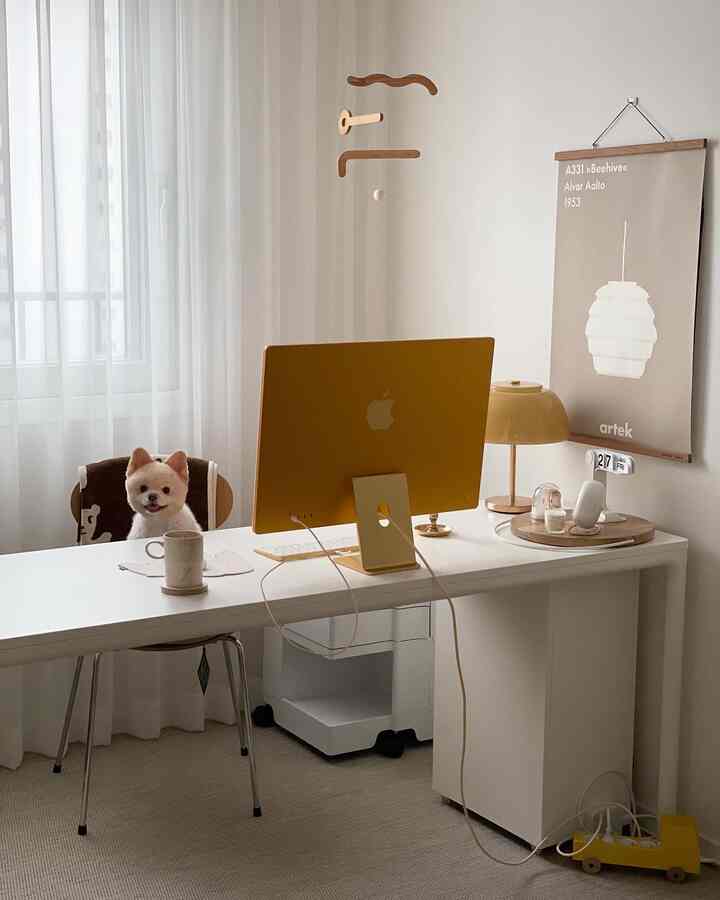 White and yellow toned home office space featuring a yellow iMac on desk center and a pet dog seated on a chair, with a bright and cozy atmosphere