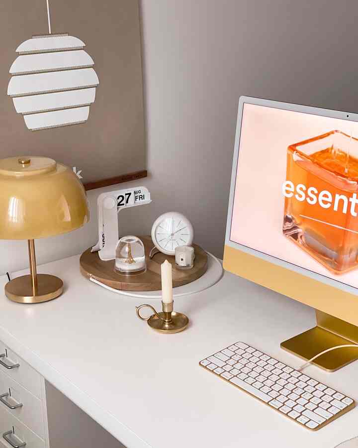 A white and gold toned home office featuring a clean desk with a table lamp, clock, and modern accessories