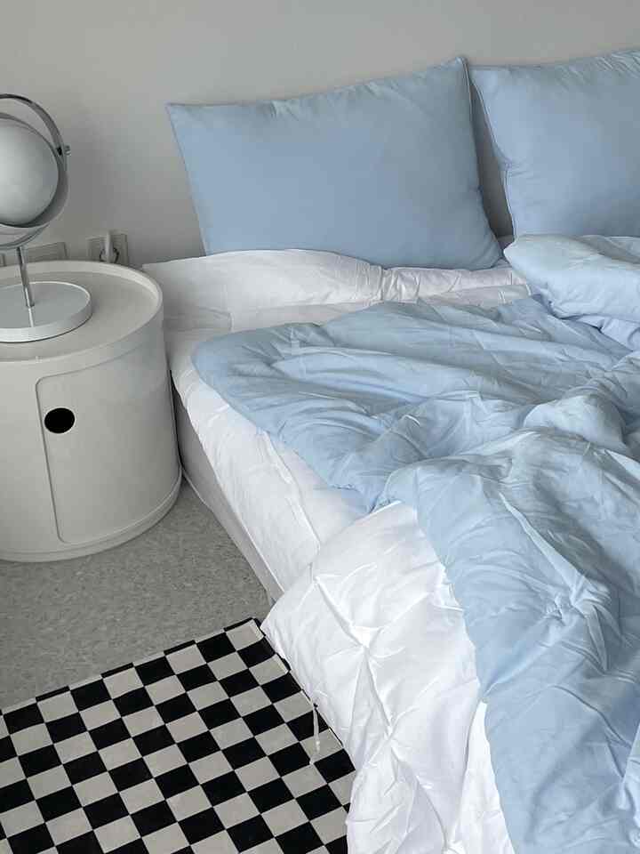 ホワイトとパステルブルーのトーンが特徴の寝室、ナイトテーブルとマットレスが配置されたシンプルで落ち着いた空間