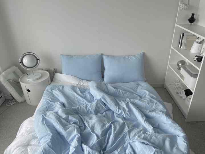 Minimal bedroom with light blue bedding and white walls and shelves creating a calm atmosphere