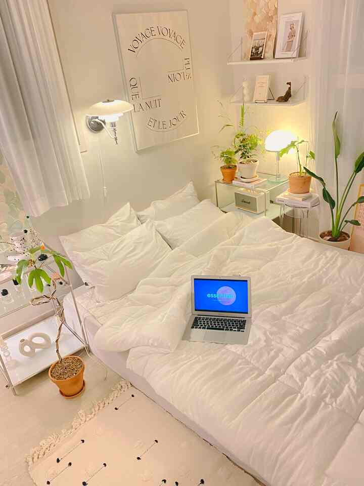 White-toned bedroom featuring bed, plants on side tables and stools, with a clean and simple atmosphere