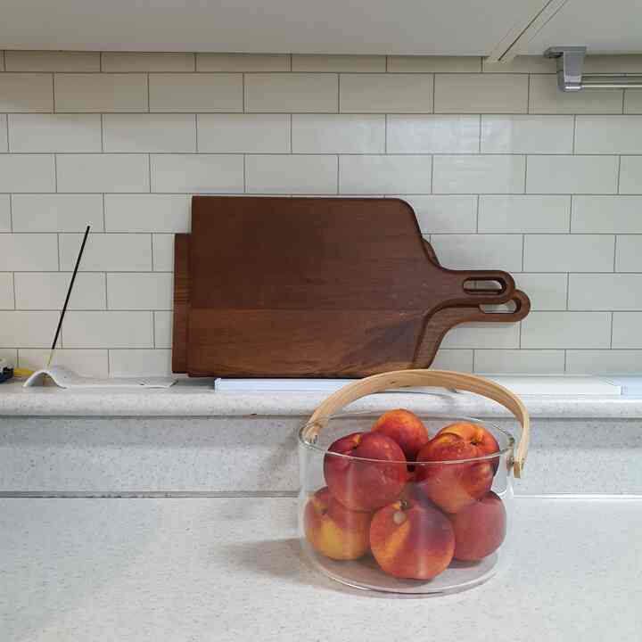 Natural-toned kitchen countertop featuring wooden cutting boards and a transparent chill basket filled with peaches in a tidy space