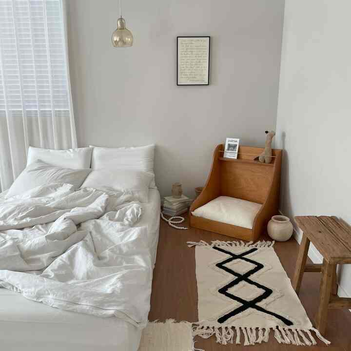 Bedroom with white and wood tone harmony featuring a white bed, rug, and wooden chair creating a simple and natural atmosphere