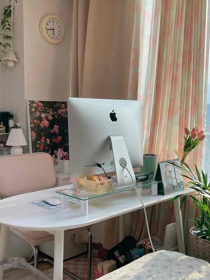 Beige toned studio workspace featuring a white desk, pink floral curtains, and plants creating a cozy remote work atmosphere