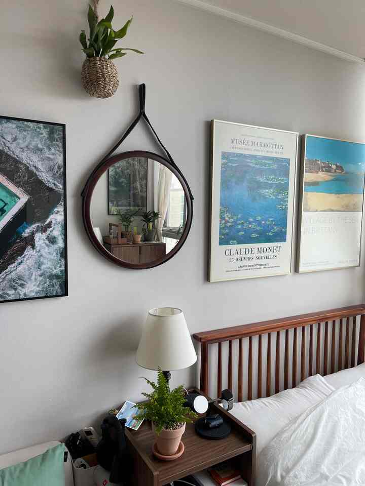 ホワイトと木目調が調和する寝室、ウォールナット製のベッドとナイトテーブル、丸いレザーの壁掛け鏡、海の風景を描いた額縁が配置された雰囲気のあるインテリア