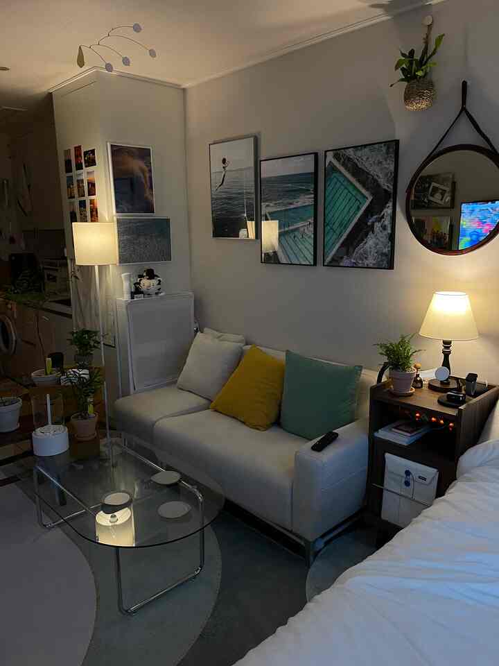 ホワイトとブルーのトーンのリビング、ホワイトのソファとガラスのコーヒーテーブル、壁の額縁や植物が配置されたモダンな雰囲気のインテリア