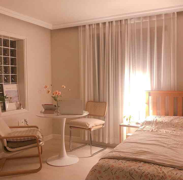 Warm wood tone and white bedroom featuring round table, rattan chair, and nightstand lighting creating a cozy atmosphere